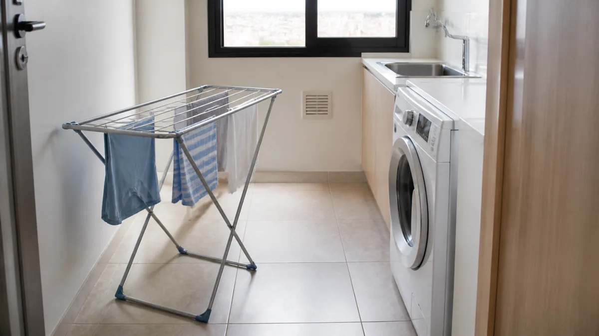 Varal de chão aberto em lavanderia pequena com máquina acessível, janela livre e passagem preservada.